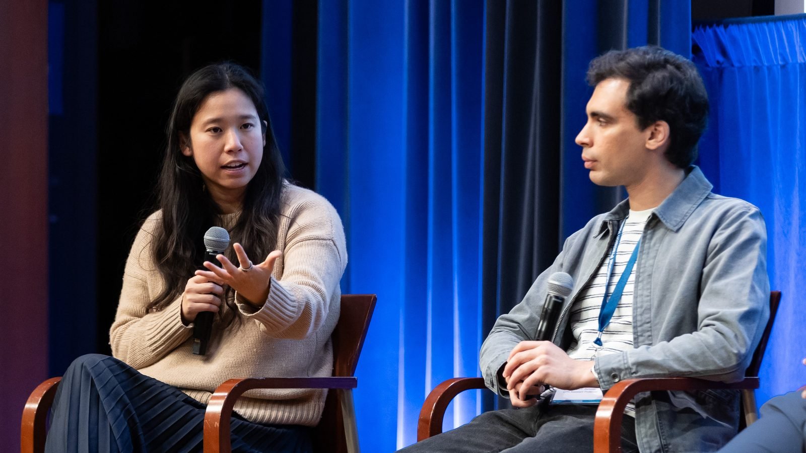 Two panelists with microphones in conversation on stage