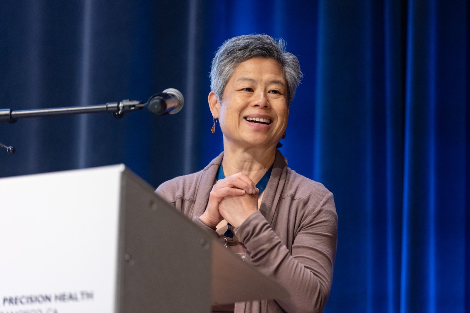 Speaker smiling at the podium on stage at a precision health conference