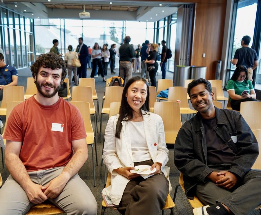 Three smiling attendees seated together among rows of chairs
