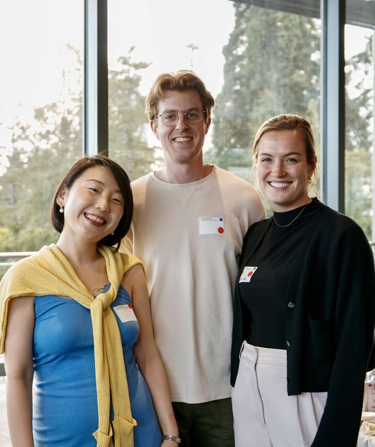 Three smiling attendees standing together in front of tall windows